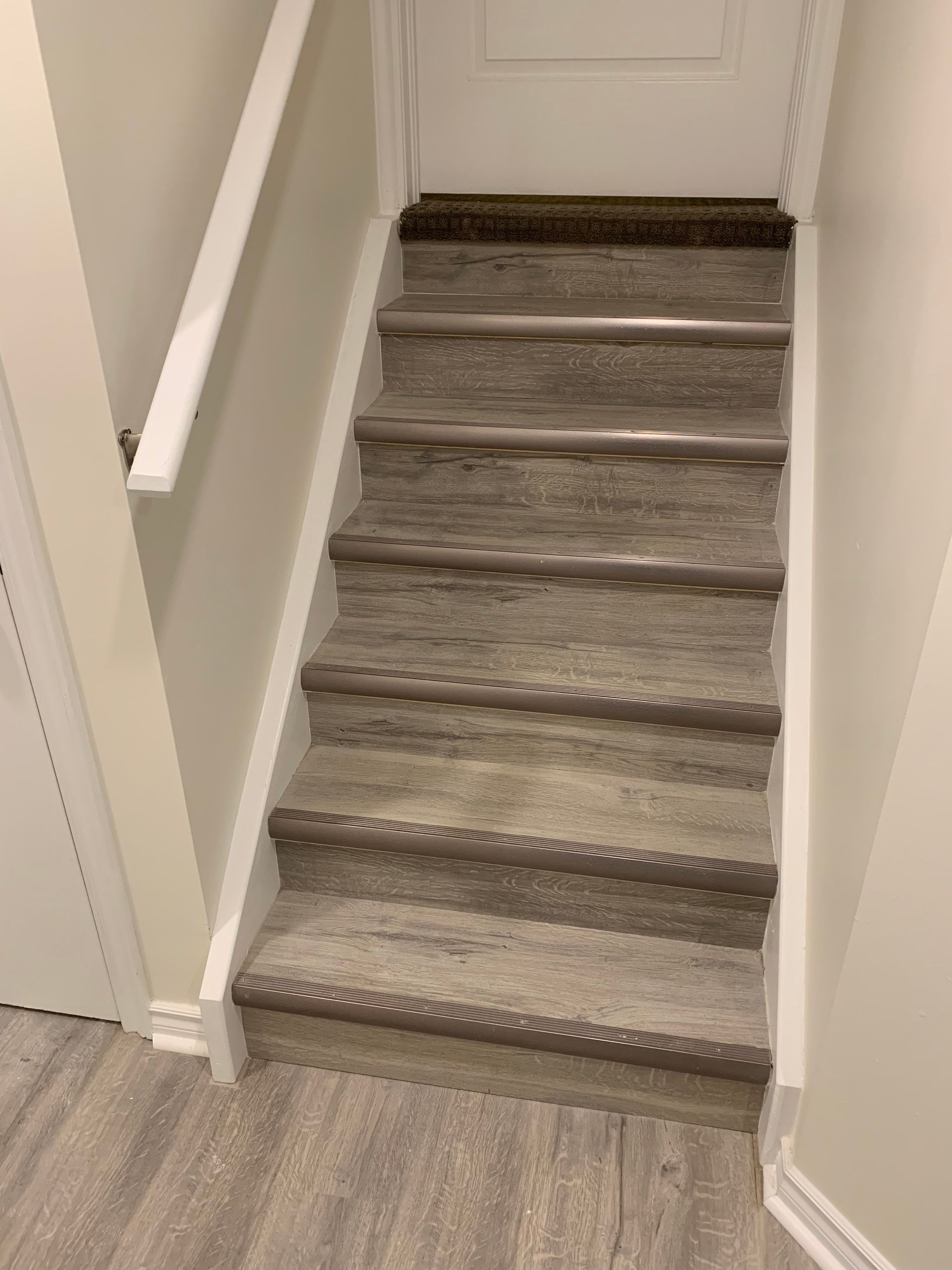 Narrow carpeted staircase with gray runner leading to a white door in a beige hallway