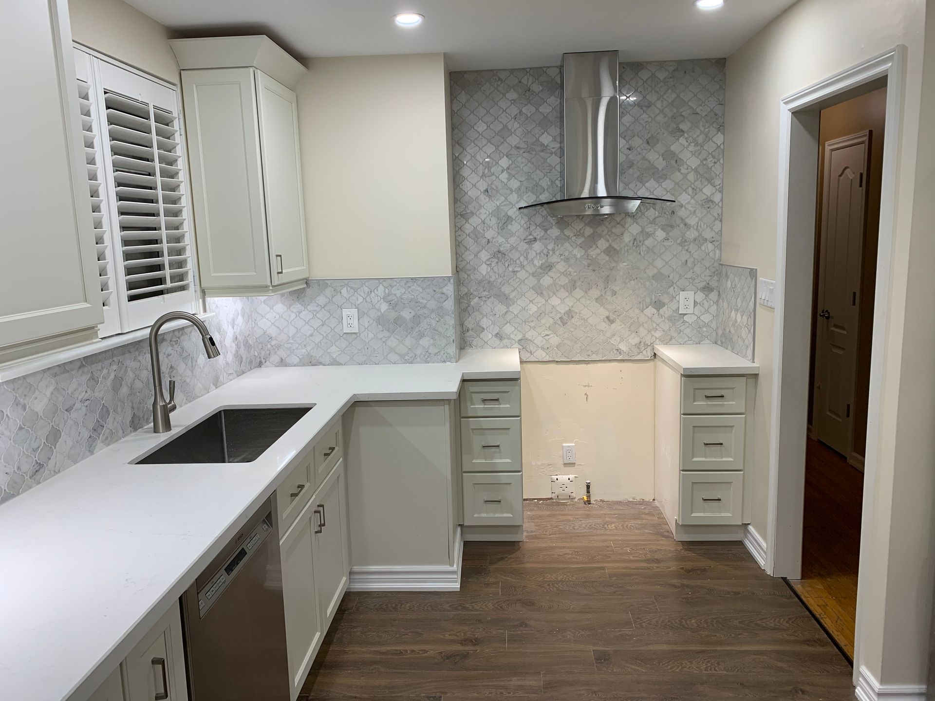Modern kitchen with white cabinets, stainless range hood, gray tile backsplash, and wood flooring.