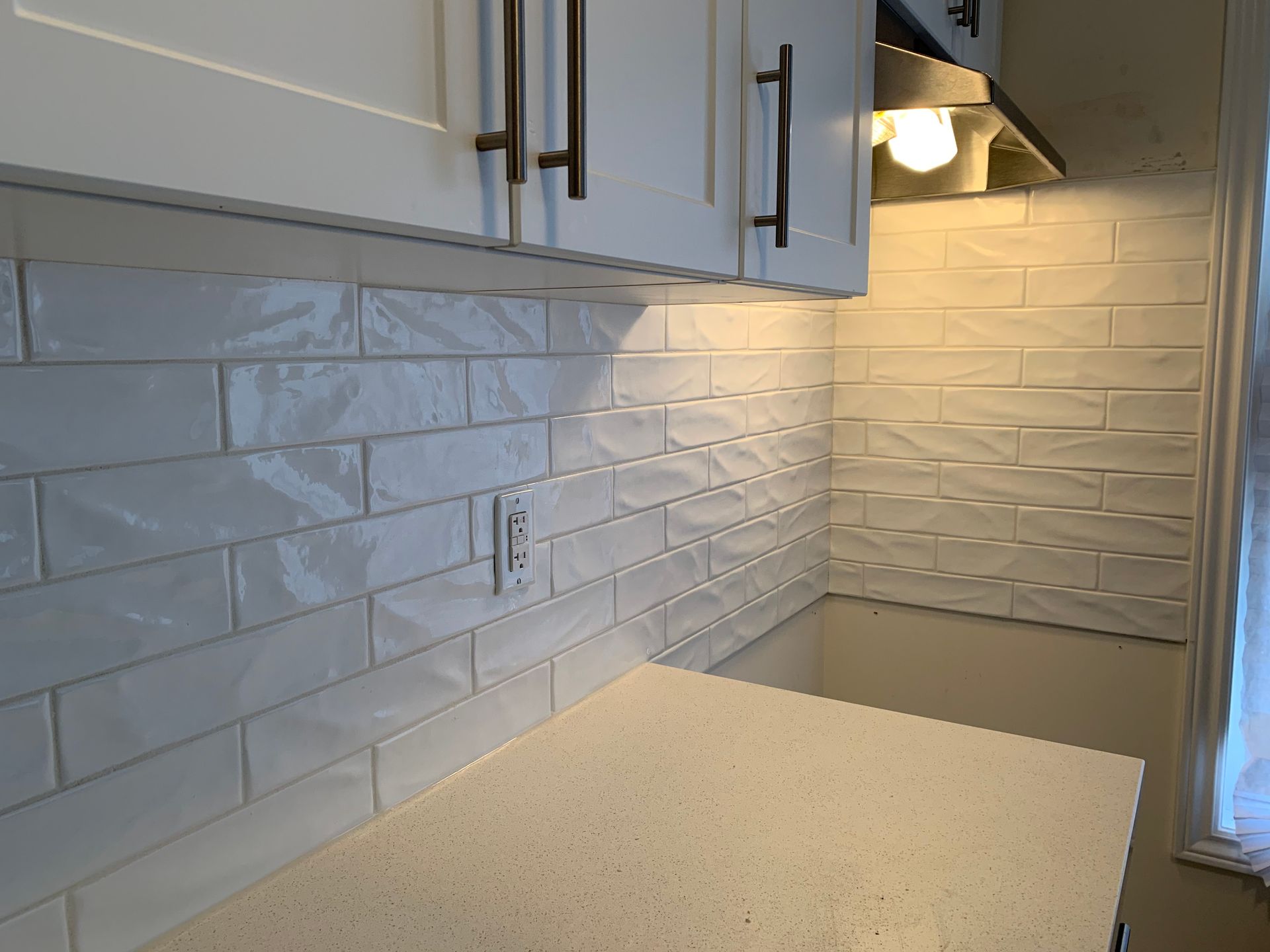 Small kitchen with white cabinets, subway tile backsplash, and light speckled countertop under a range hood