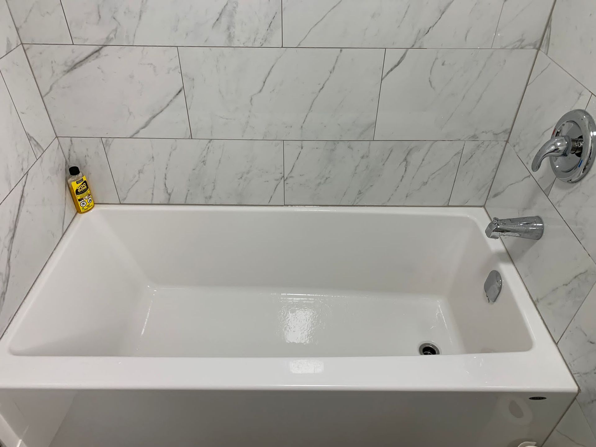 Empty white bathtub with marble tile walls and a wall-mounted faucet in a bathroom.