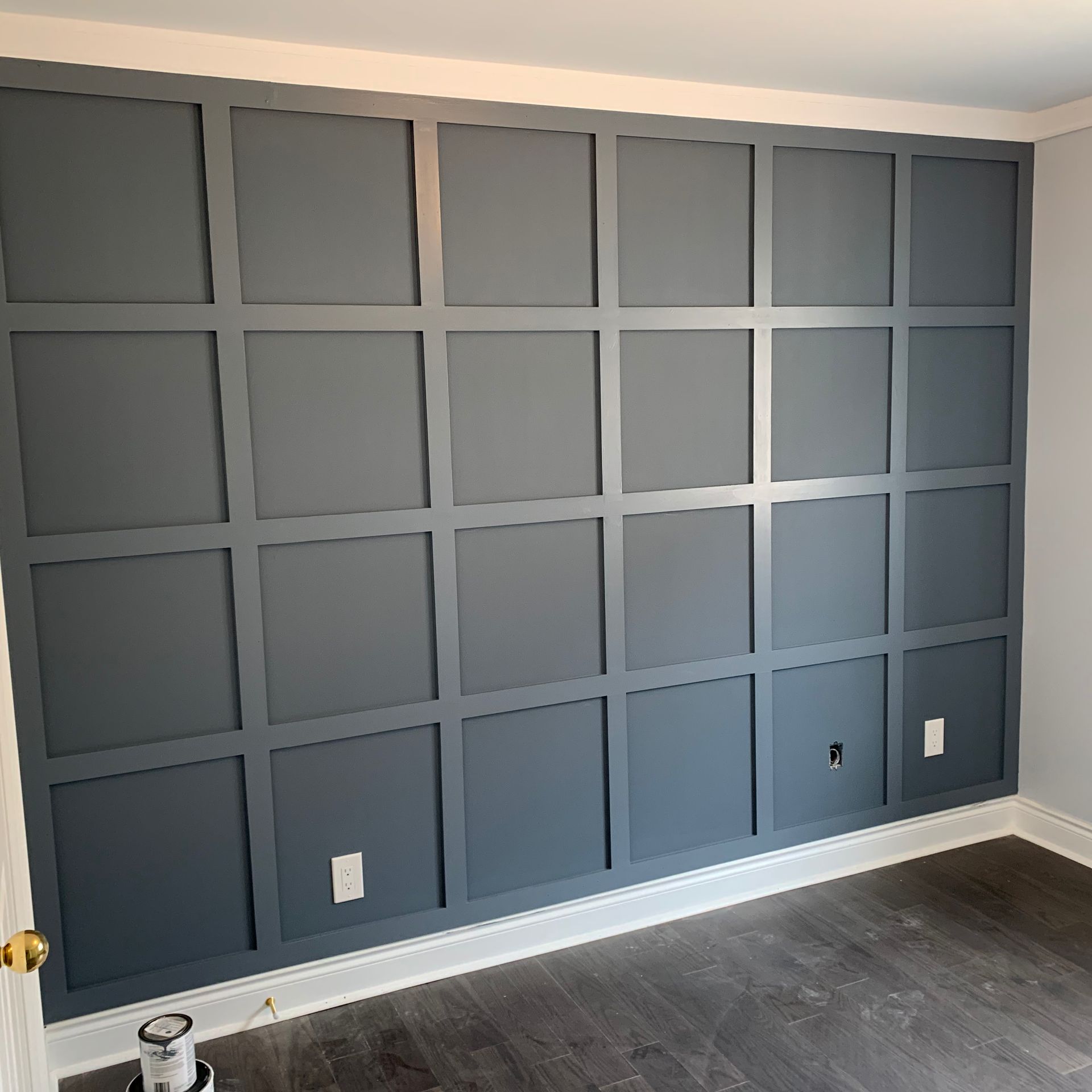 Gray paneled accent wall in an empty room with dark wood floor and white trim