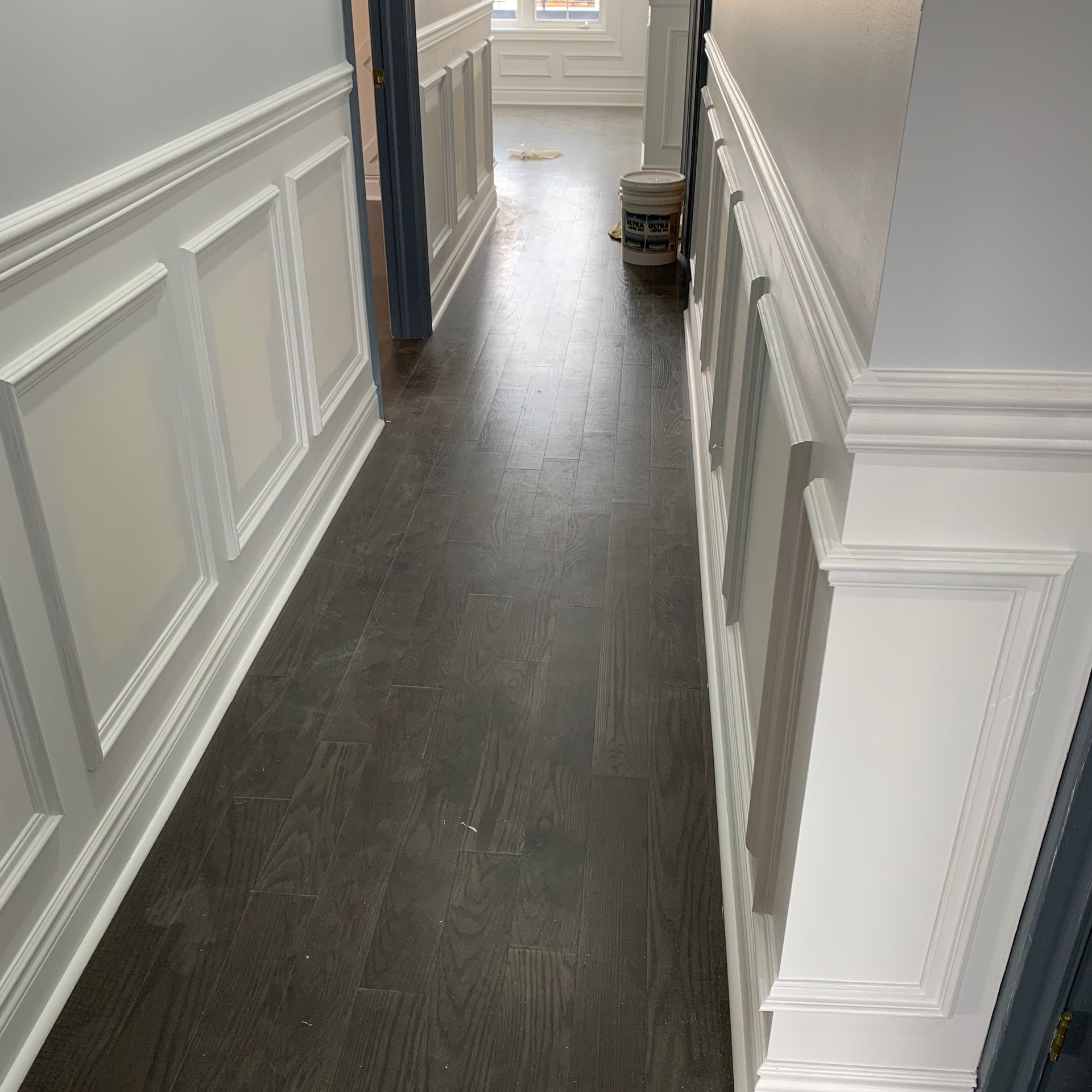 Narrow hallway with dark wood floors, white wainscoting, and a window at the far end