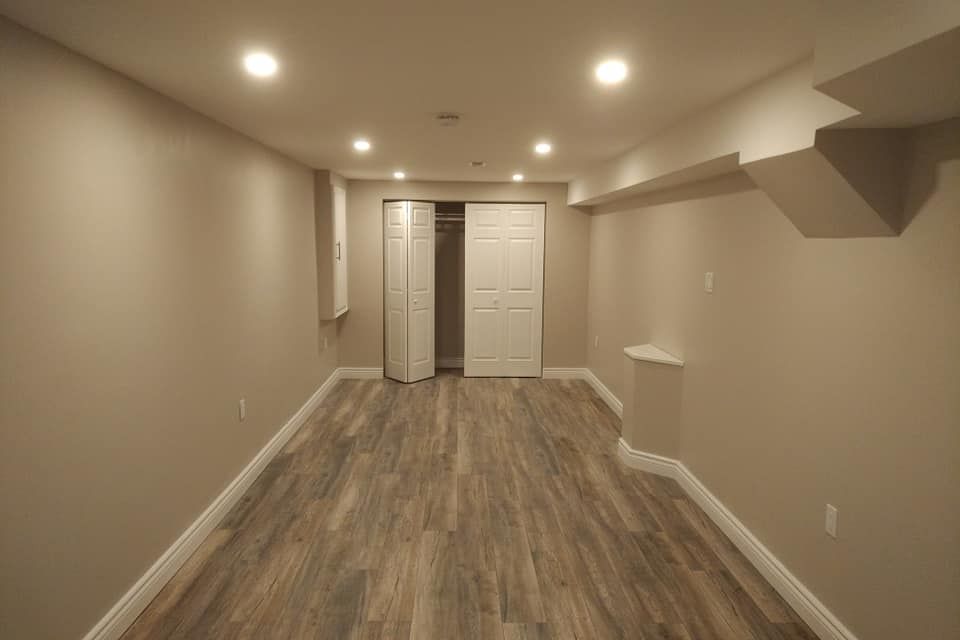 Empty finished basement with recessed lights, wood-look flooring, and a double-door closet at the far end