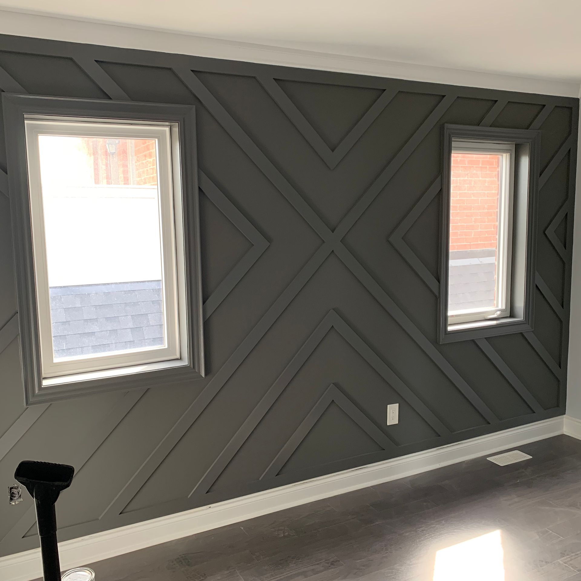 Dark gray accent wall with geometric paneling and two small windows in a sunlit room