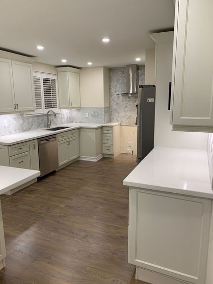 Bright white kitchen with marble countertops, gray cabinets, and dark wood floor in a modern home.