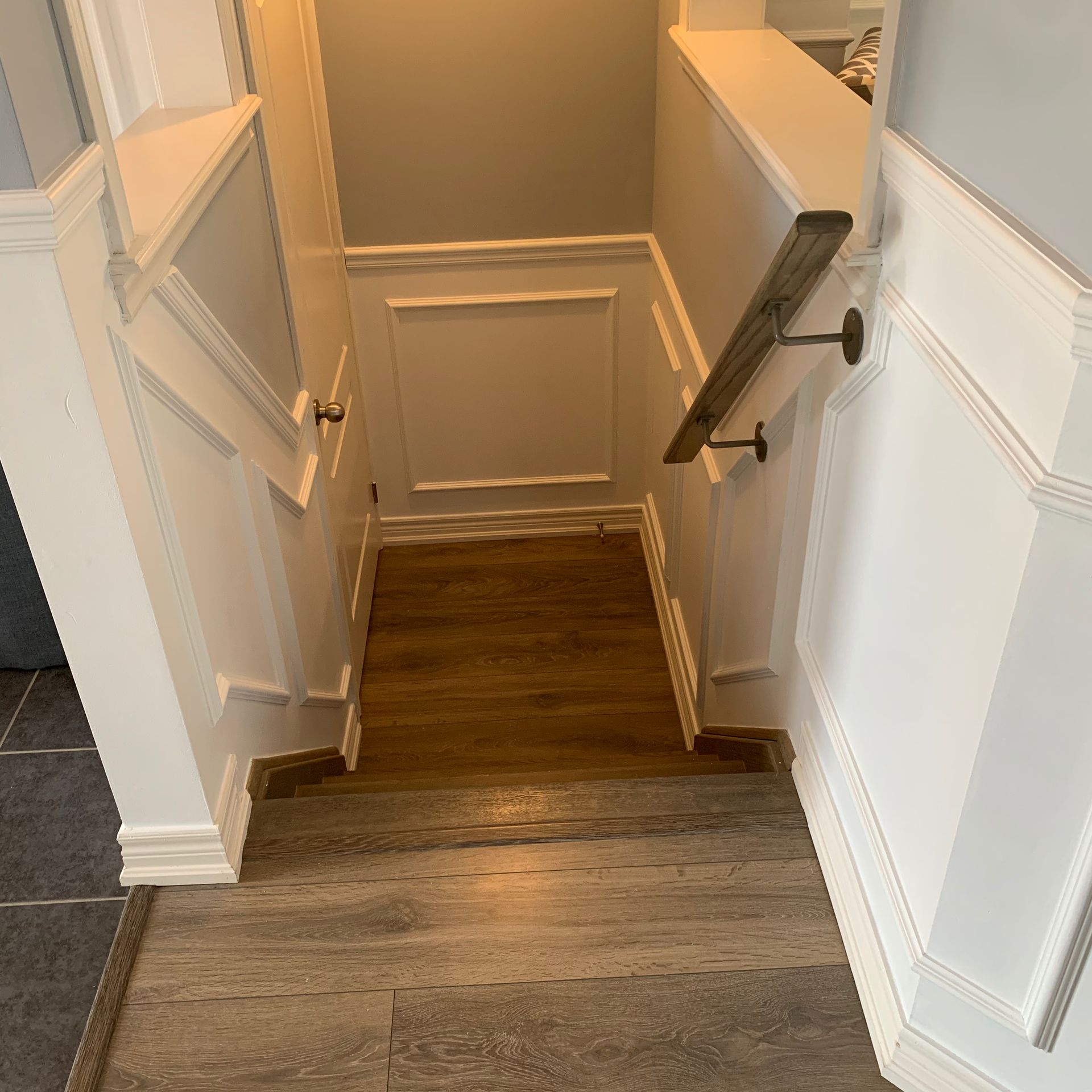 Wooden stairwell descending to a lower level with white walls and dark handrails