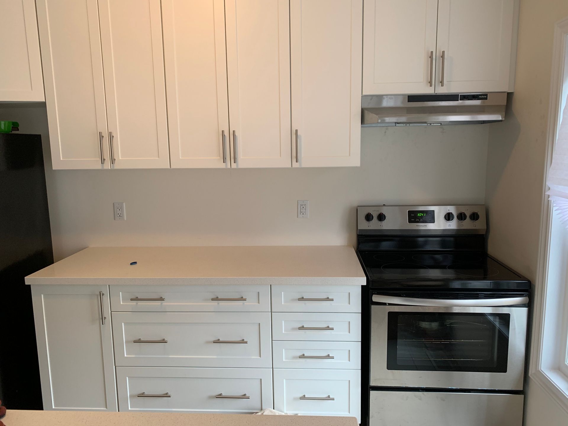 Small kitchen with white cabinets, beige countertops, and a black-and-silver stove.
