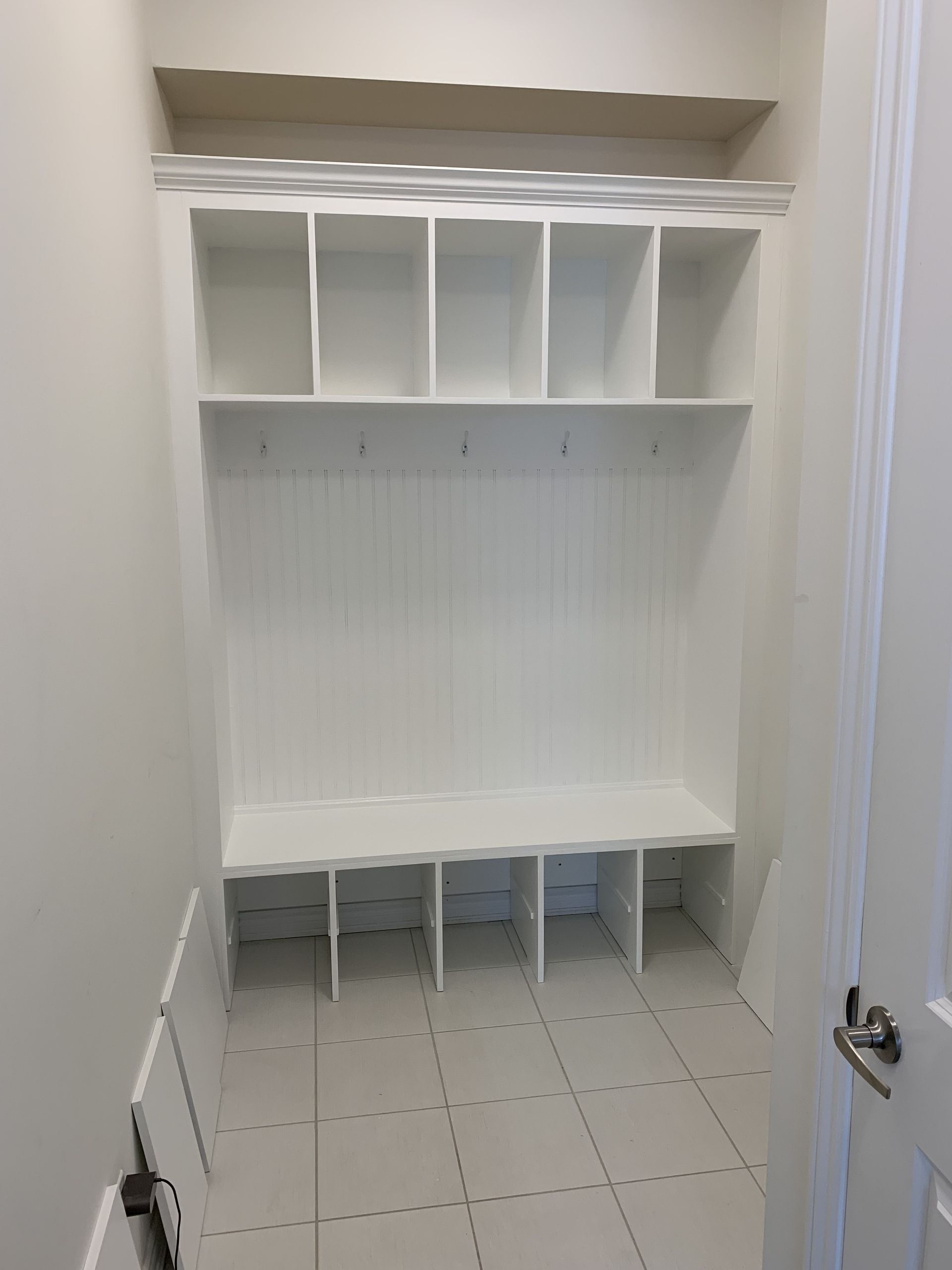 White built-in cubby storage and bench in a small room with tiled floor