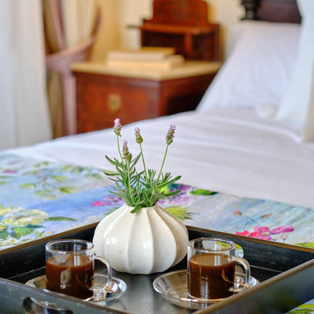 Tray with coffee and a vase of flowers on a bed with floral bedding.