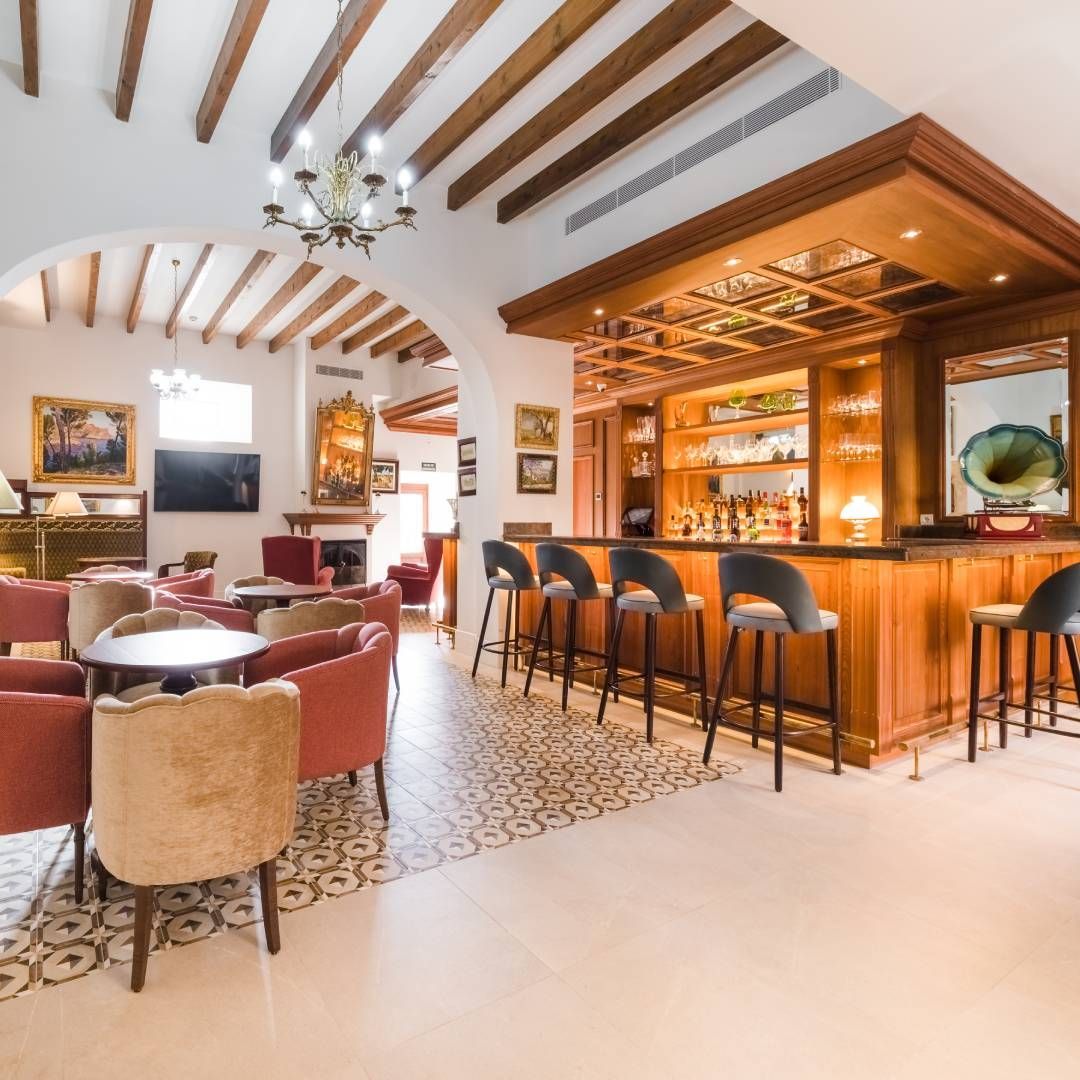 Bar with wooden counter, stools, and seating area. Arched doorway, ornate ceiling.