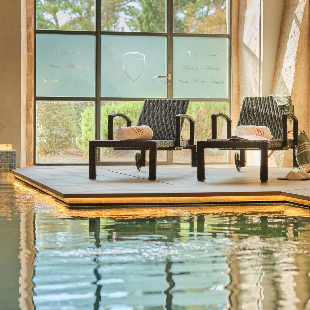 Two chairs with towels by a pool with a window.