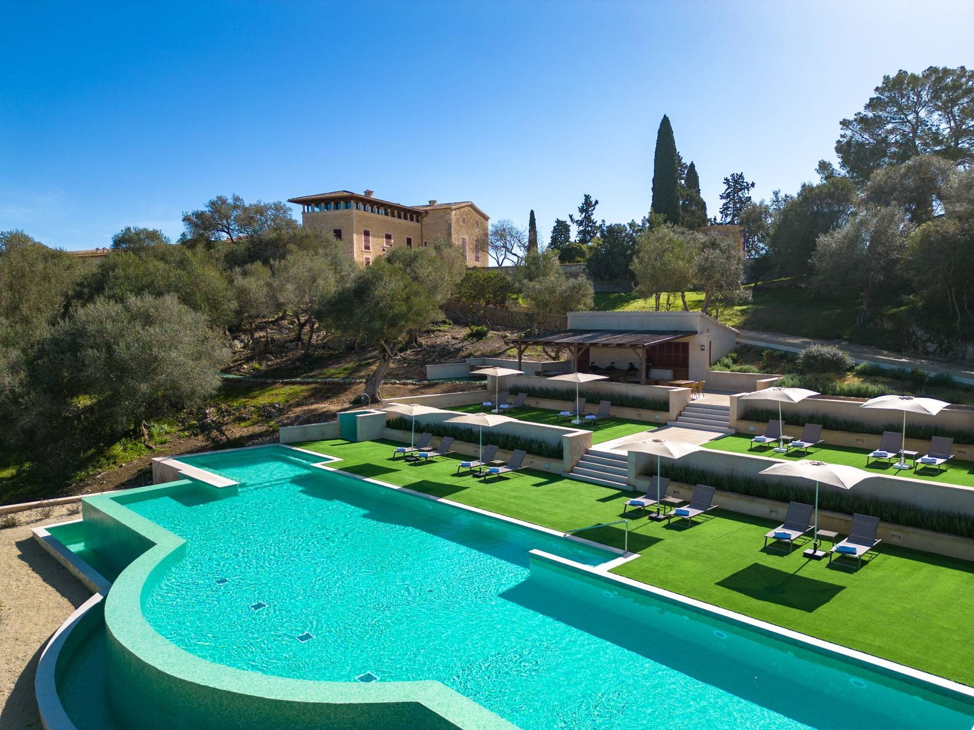 Luxury hotel pool with lounge chairs, umbrellas, and stone building in background.