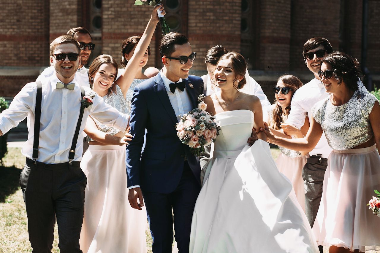 Wedding bouquet in focus; blurred couple kissing in the background. White roses and green accents.