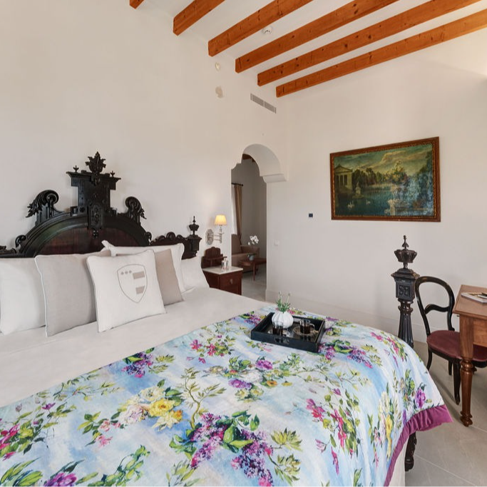 Bedroom with floral bedspread, ornate headboard, wooden beams, and arched doorway to a hallway.