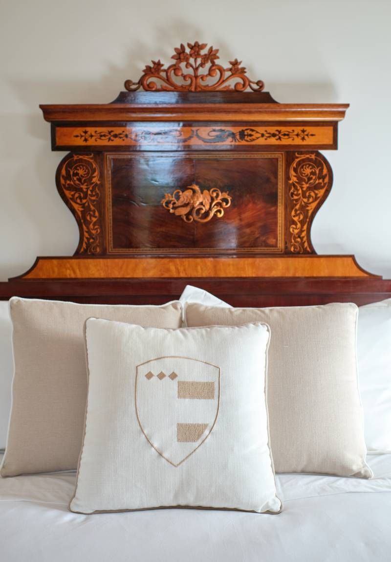 Bed with ornate wooden headboard and pillows, one with embroidered crest.