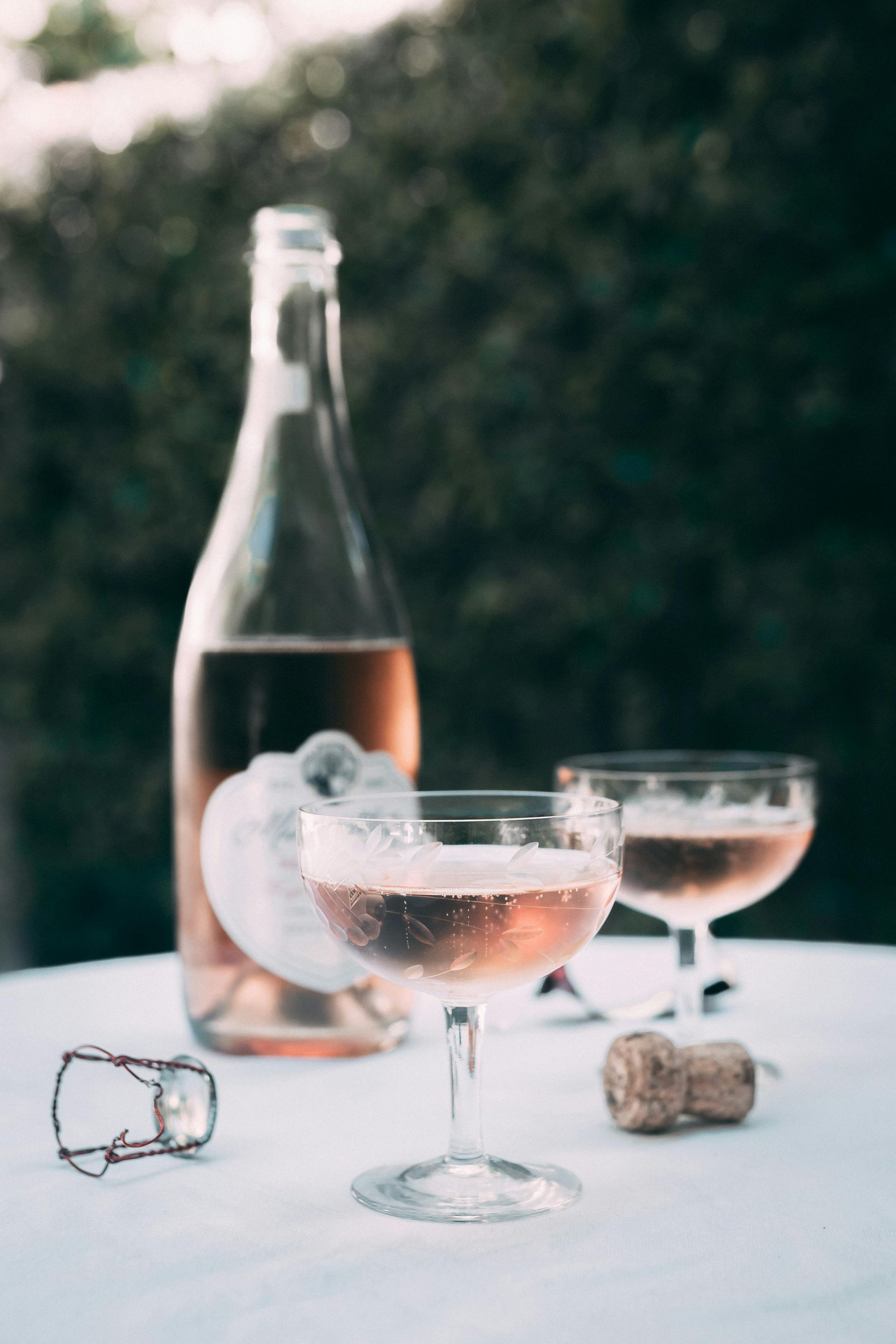 Bottle and glasses of rosé on a white tablecloth; a celebratory toast with a cork and cap.