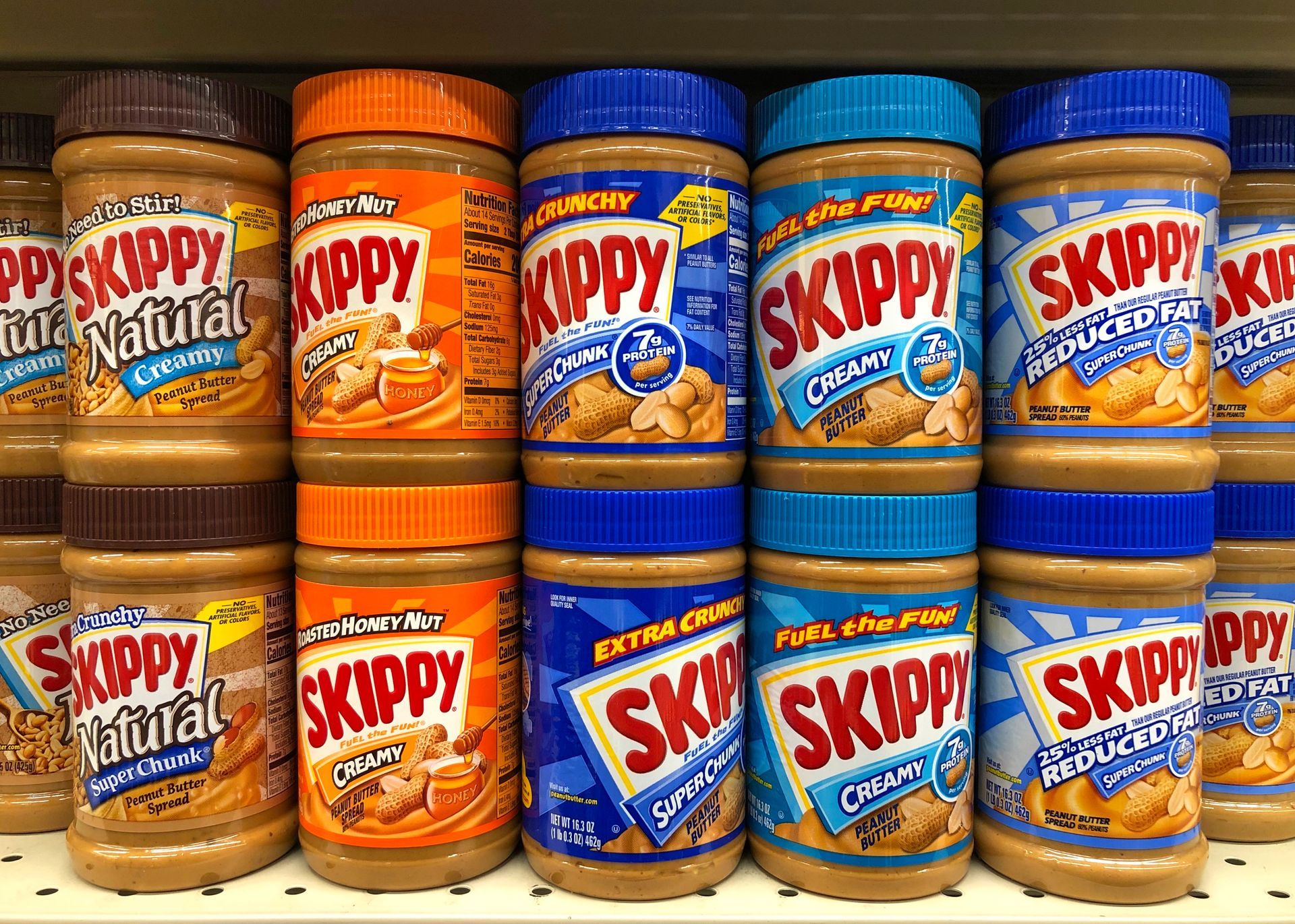 A shelf filled with bottles of skippy peanut butter in different flavors.