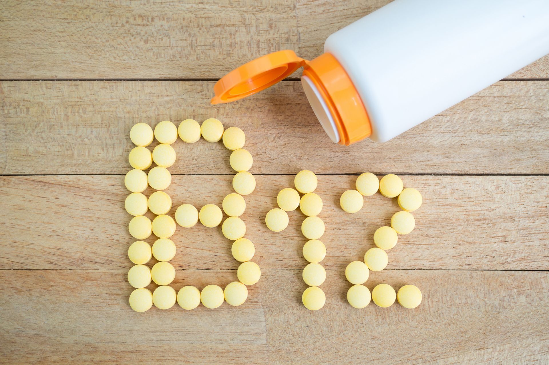 A bottle of vitamin b12 is spilling out of a bottle on a wooden table.