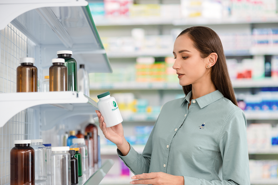 A woman is looking at a bottle of pills in a pharmacy.