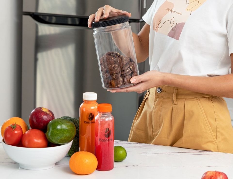 A woman is holding a jar of food in front of a bowl of fruit and juice.