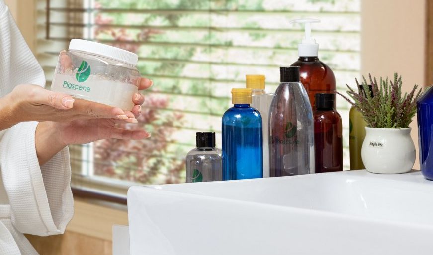 A woman in a bathrobe is washing her hands in front of a sink filled with bottles