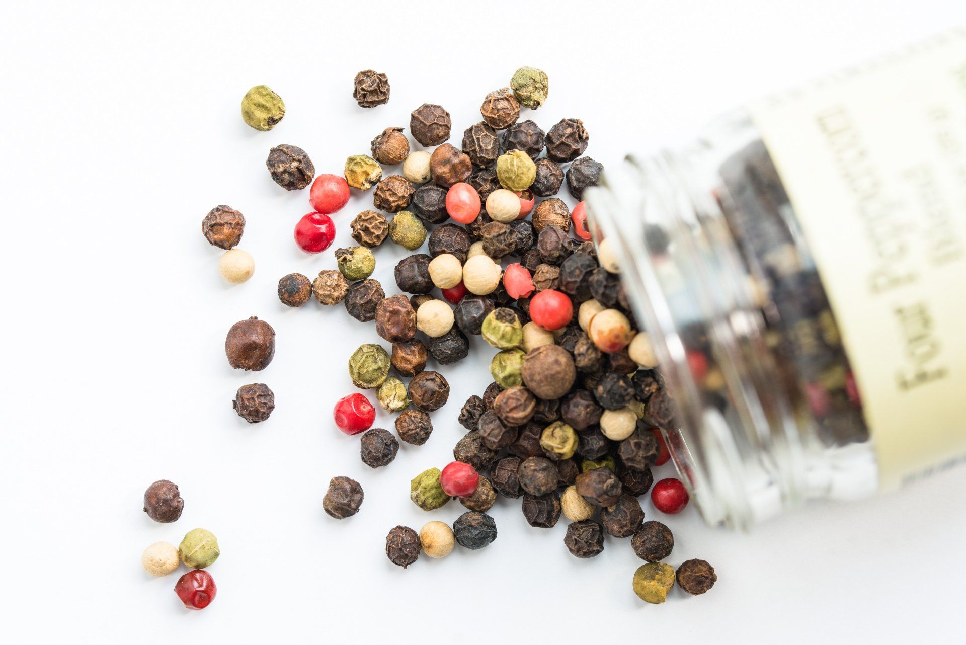 Peppercorns pouring out of a clear plastic jar.