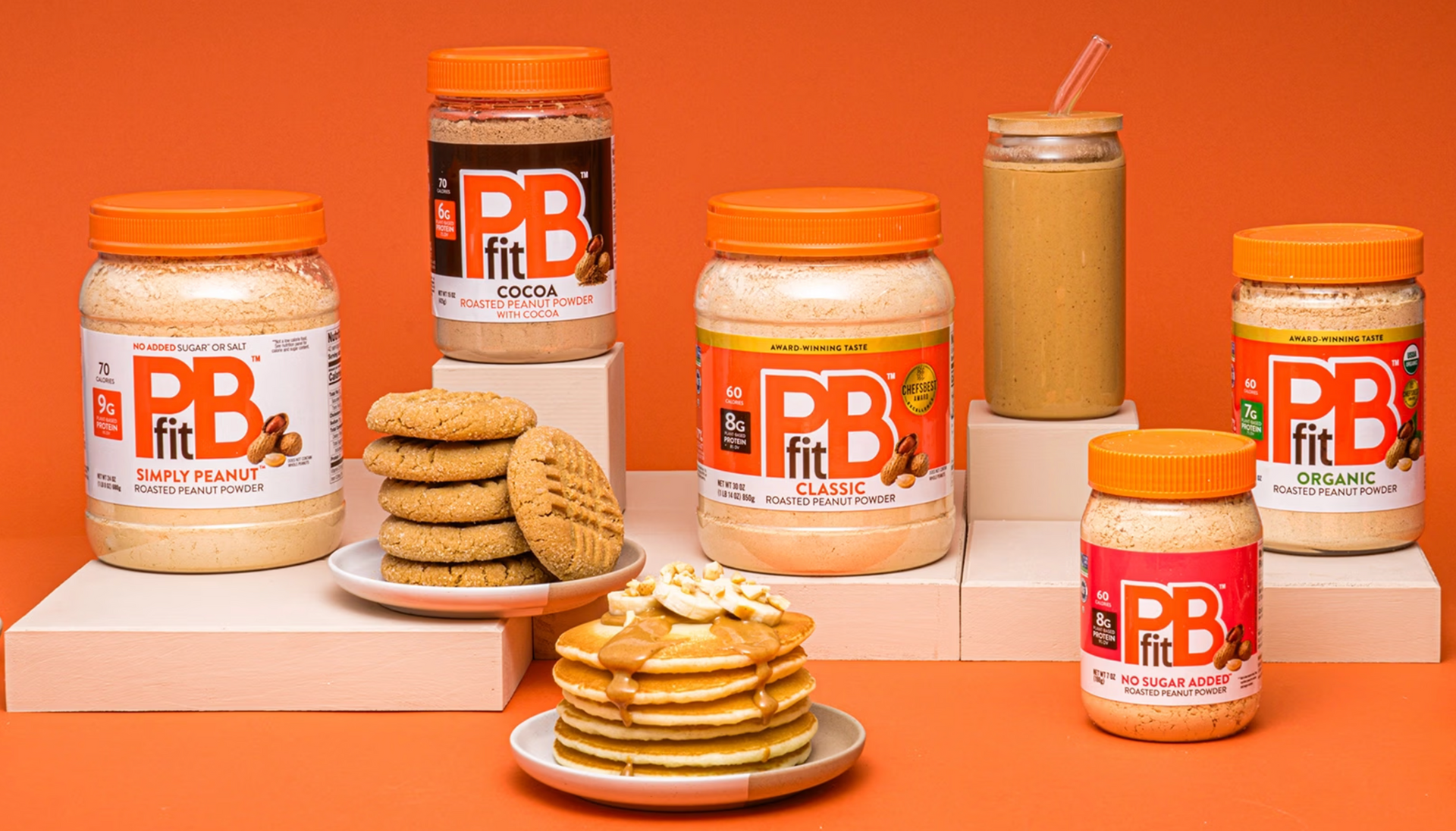 A stack of pancakes sits on top of a plate next to jars of peanut butter.