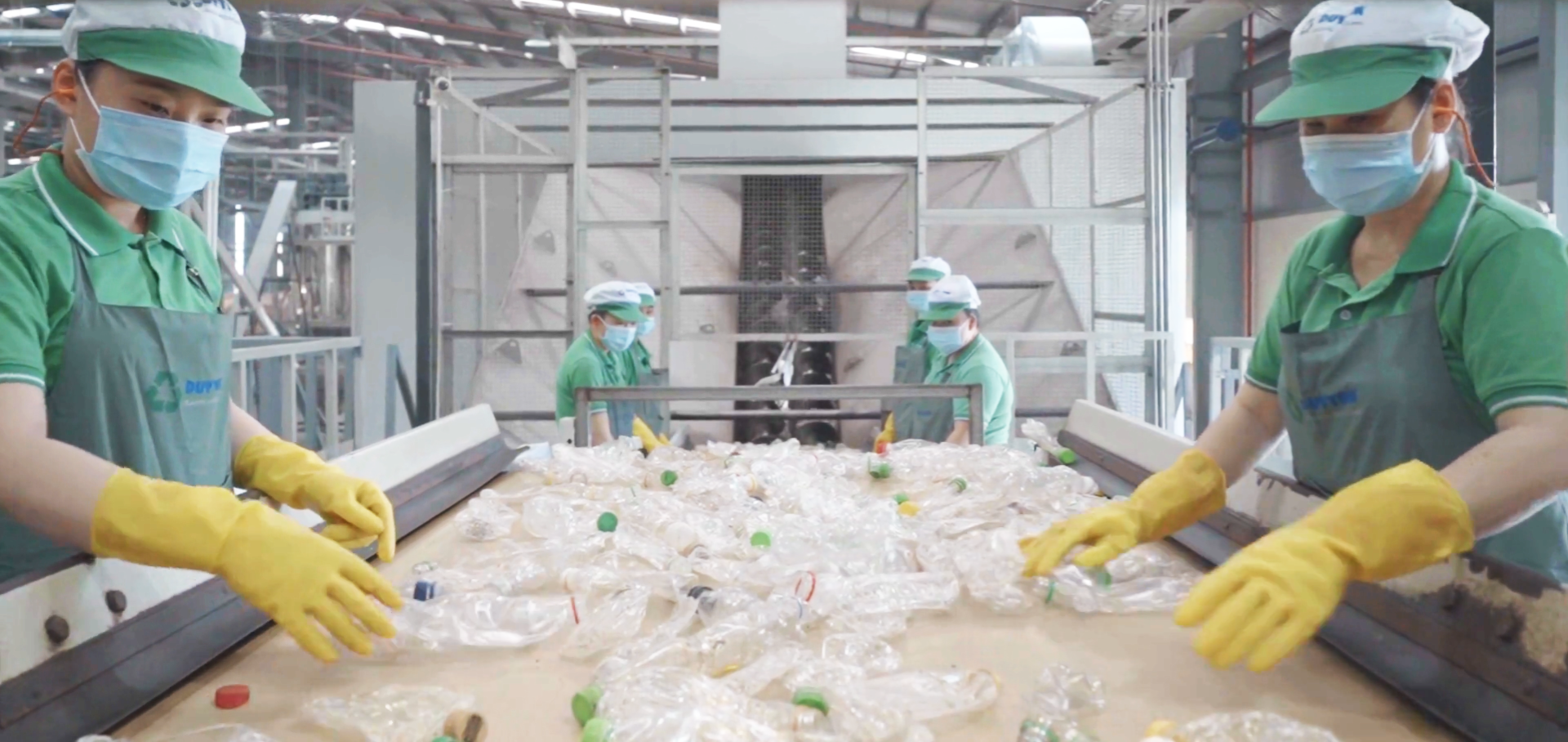 A group of people are working in a factory sorting plastic bottles on a conveyor belt.