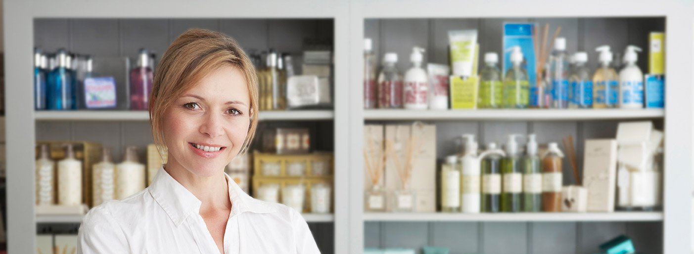 Beautician standing in front of a shelf of cosmetics and beauty products packaged in recycled plastic.