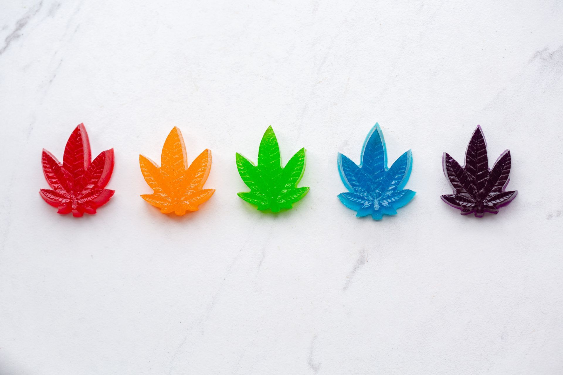 CBD gummies (shaped like cannabis leaves) in red, orange, green, blue, and purple.