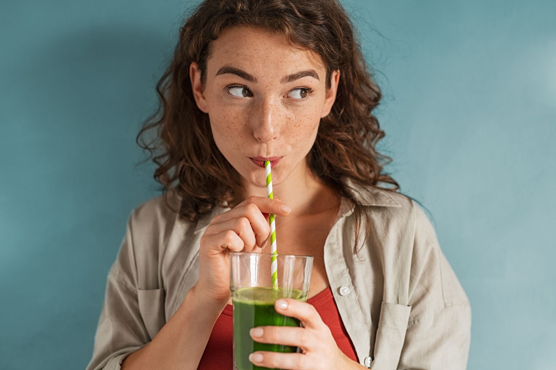 Young woman sipping cold-pressed juice through a straw.