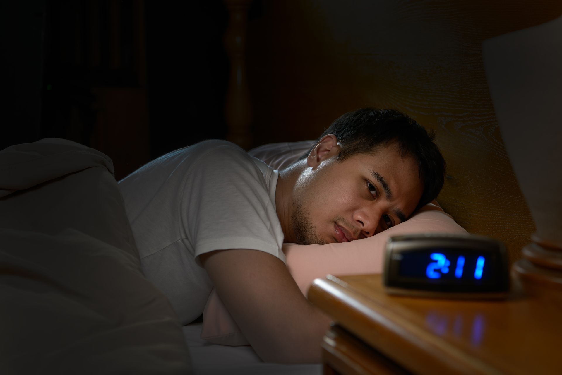 Man with insomnia lying in bed and staring at clock, which reads 