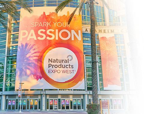 A large billboard for natural products expo west is hanging on the side of a building.