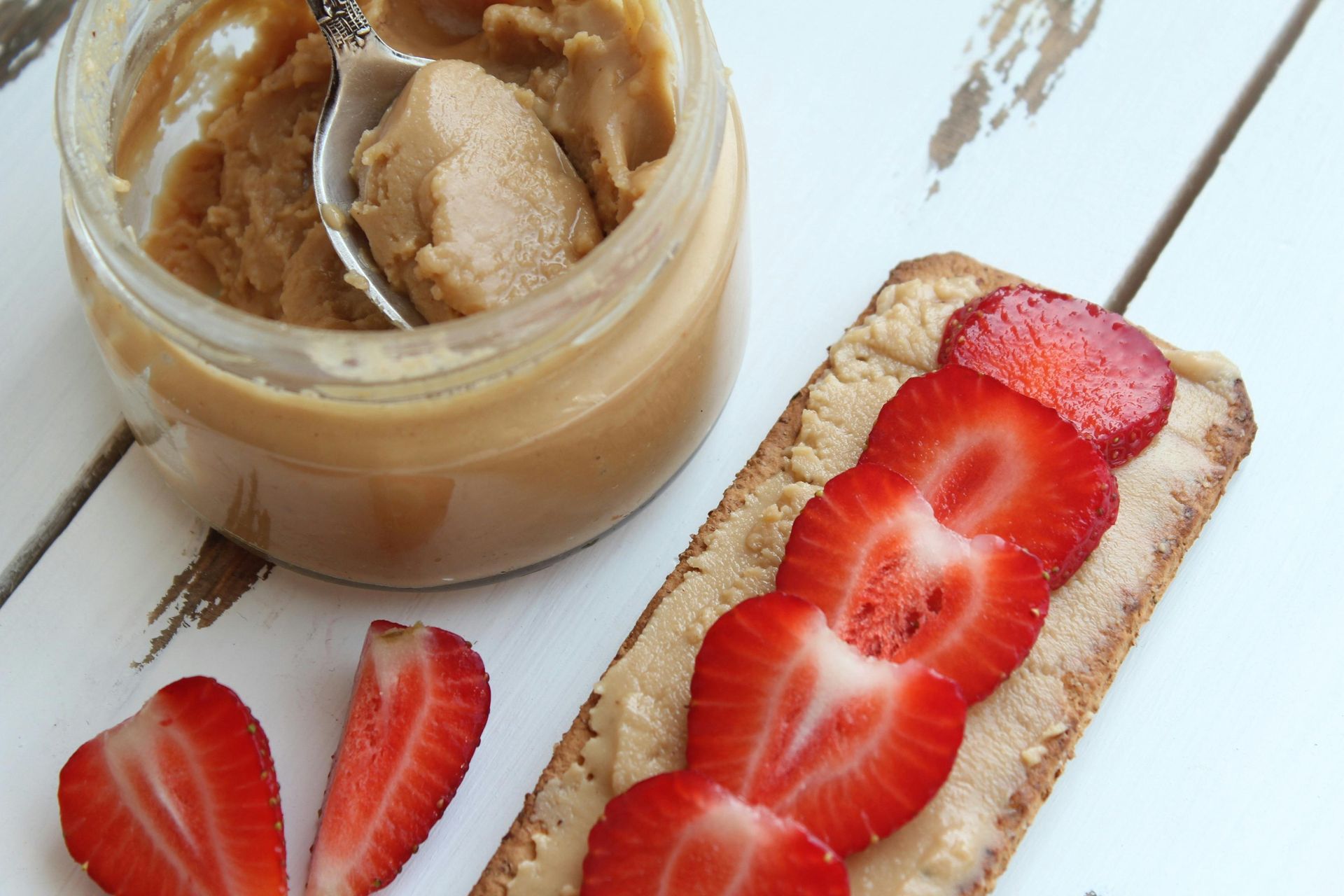A cracker with peanut butter and strawberries on it next to a jar of peanut butter.