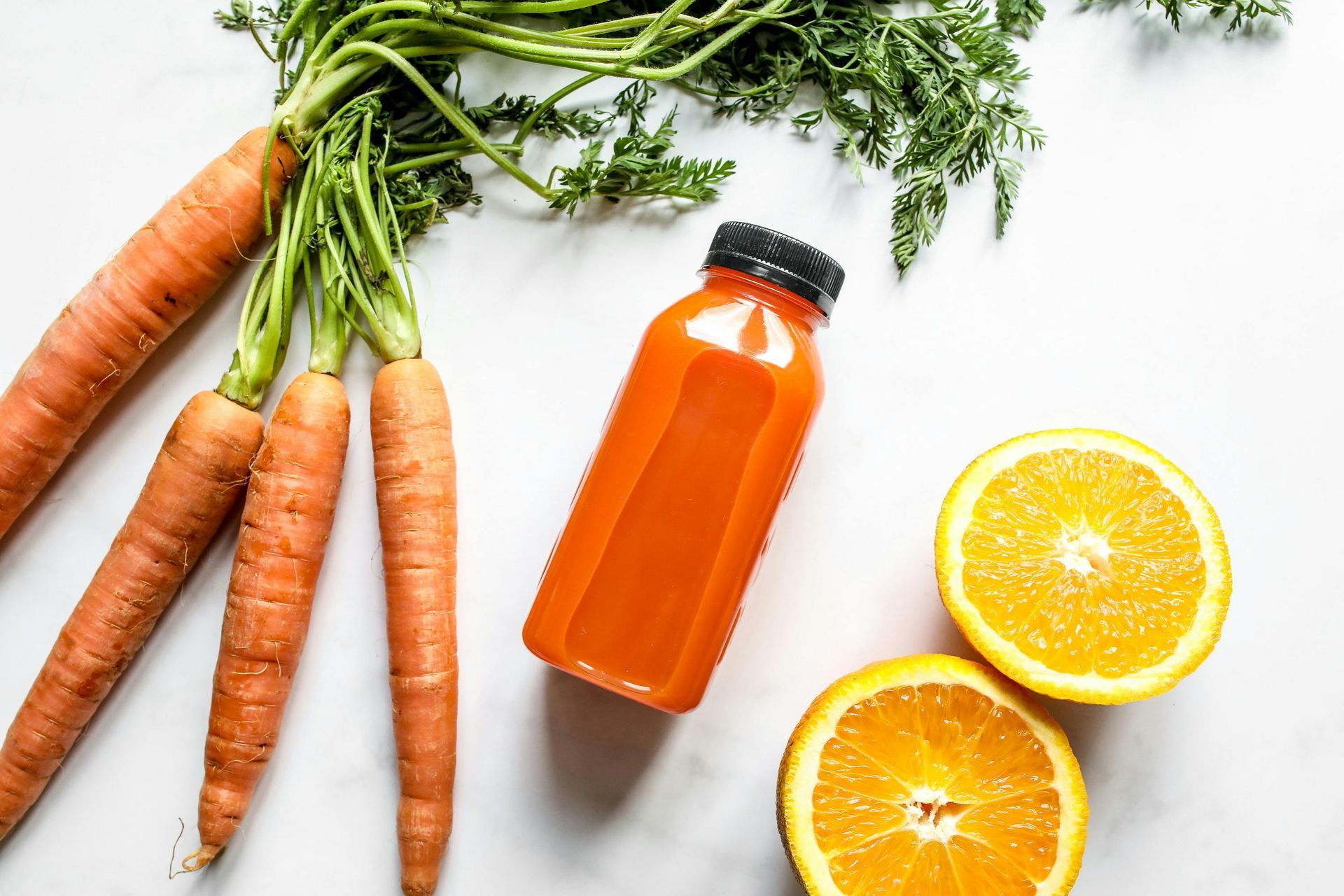 Carrots , oranges and a bottle of orange juice on a table.