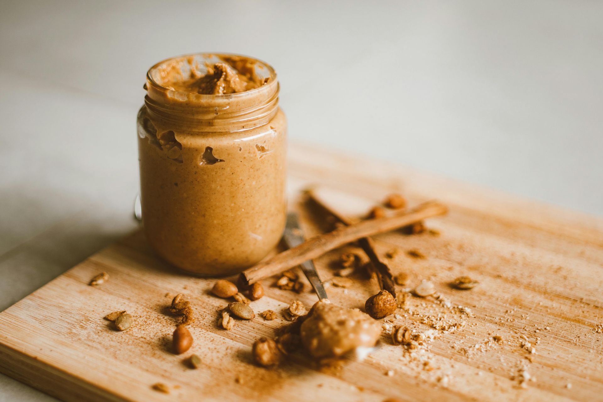 A jar of peanut butter is sitting on a wooden cutting board.