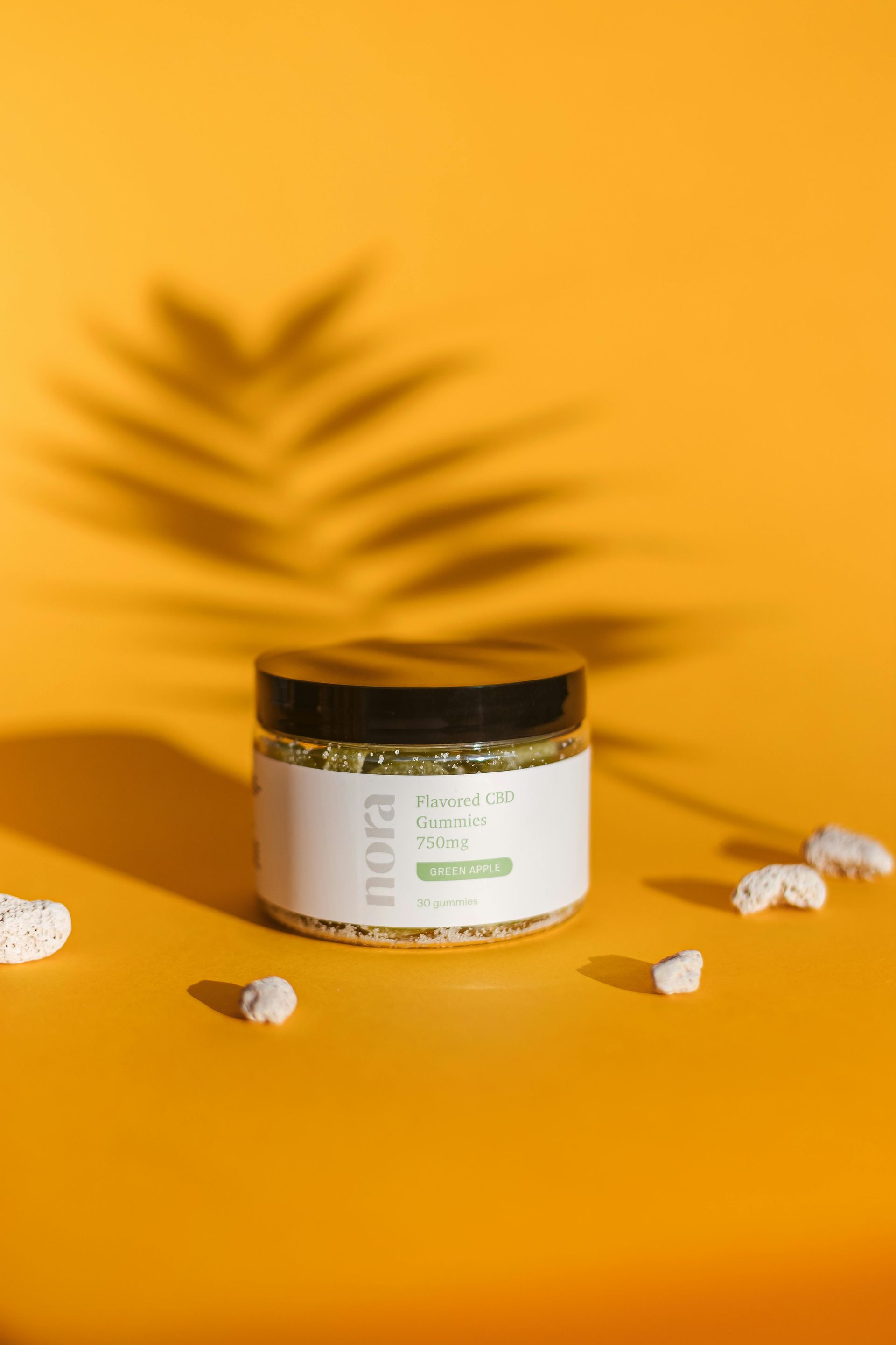 A jar of pills is sitting on a yellow table next to a palm tree leaf.