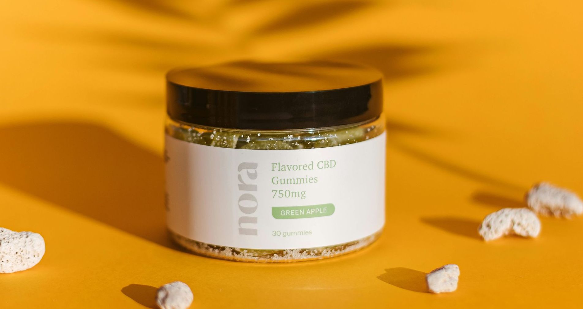 A jar of pills is sitting on a yellow table next to a palm tree leaf.
