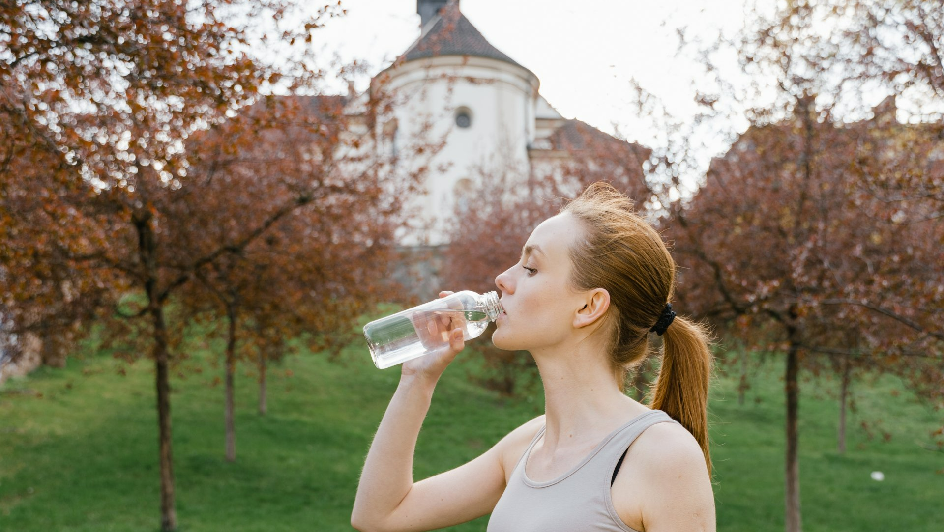Young woman runner drinking bottled water from plastic bottle.