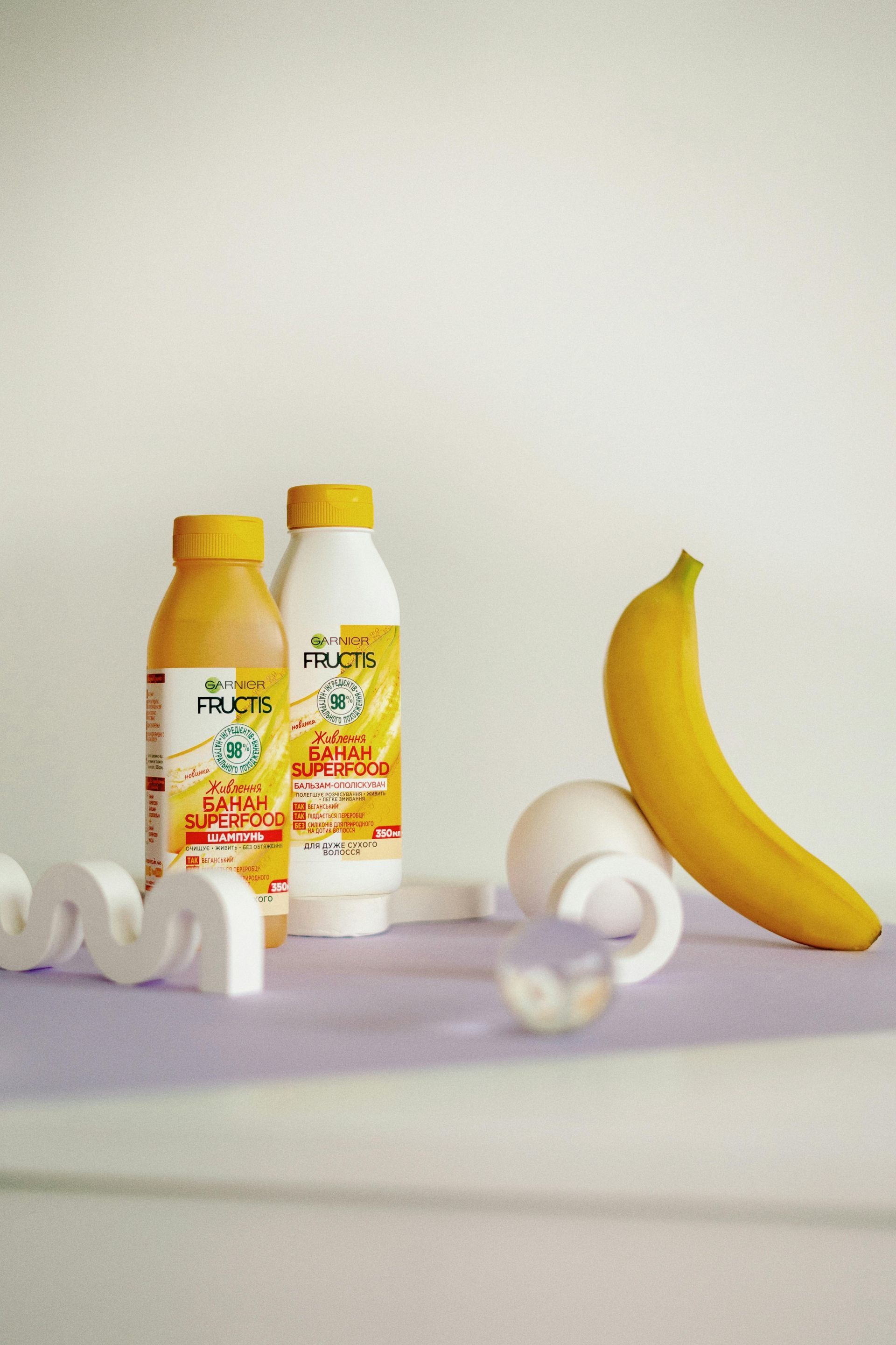Two bottles of shampoo and conditioner next to a banana on a table.