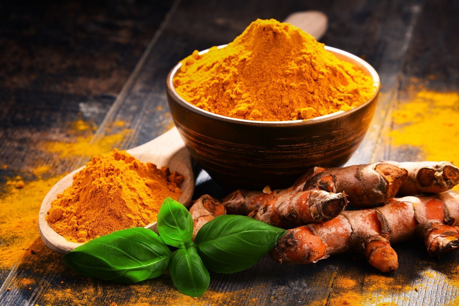 A bowl of turmeric powder along with pieces of turmeric root.