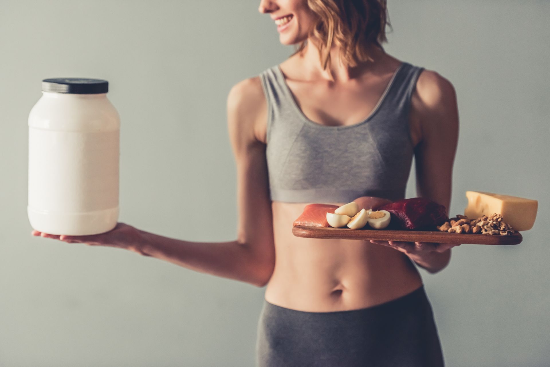Athletic woman comparing a tray of protein food to a plastic jar of protein powder.
