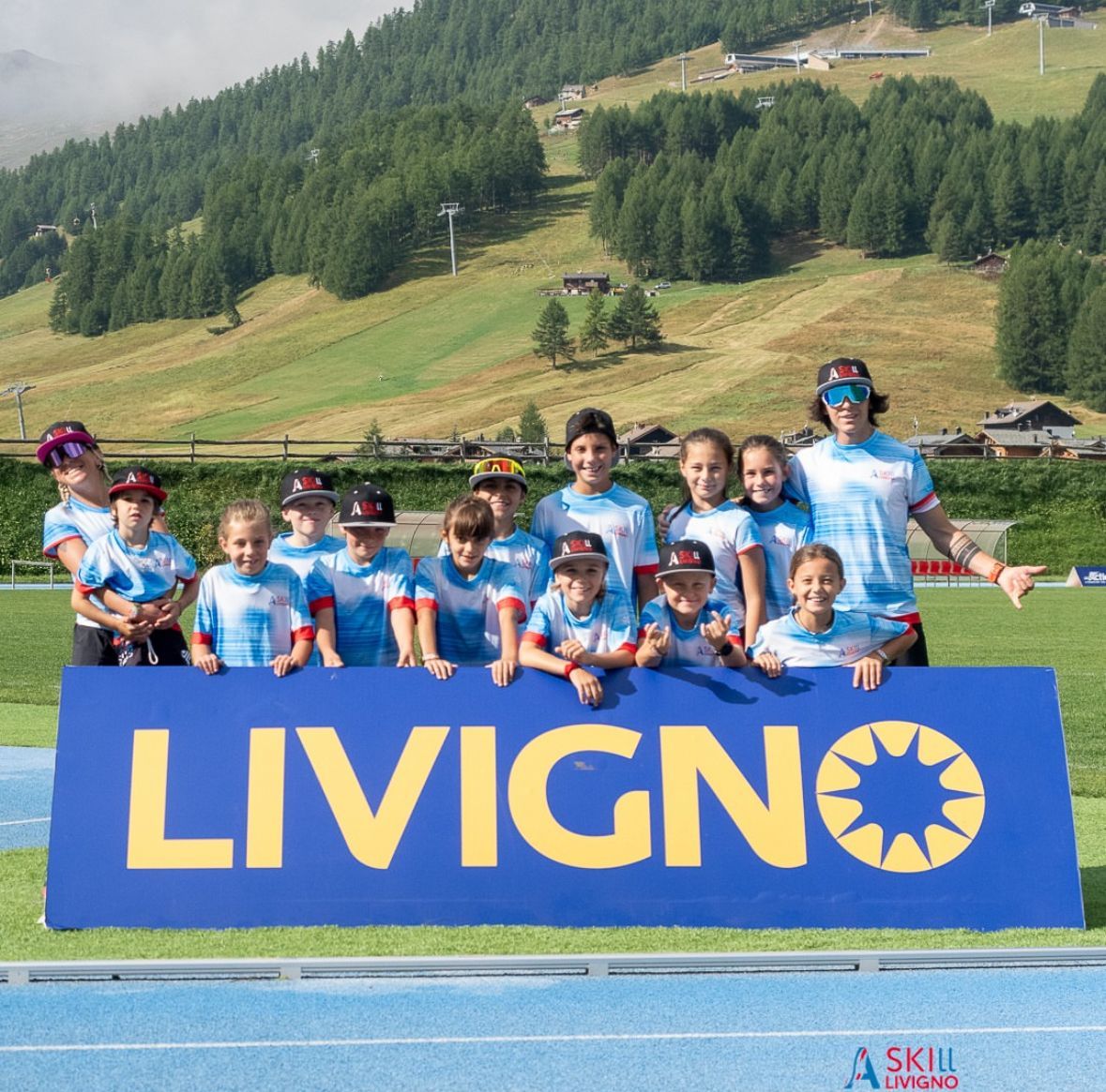 Un gruppo di bambini e un allenatore in divisa blu stanno dietro un cartello con la scritta 