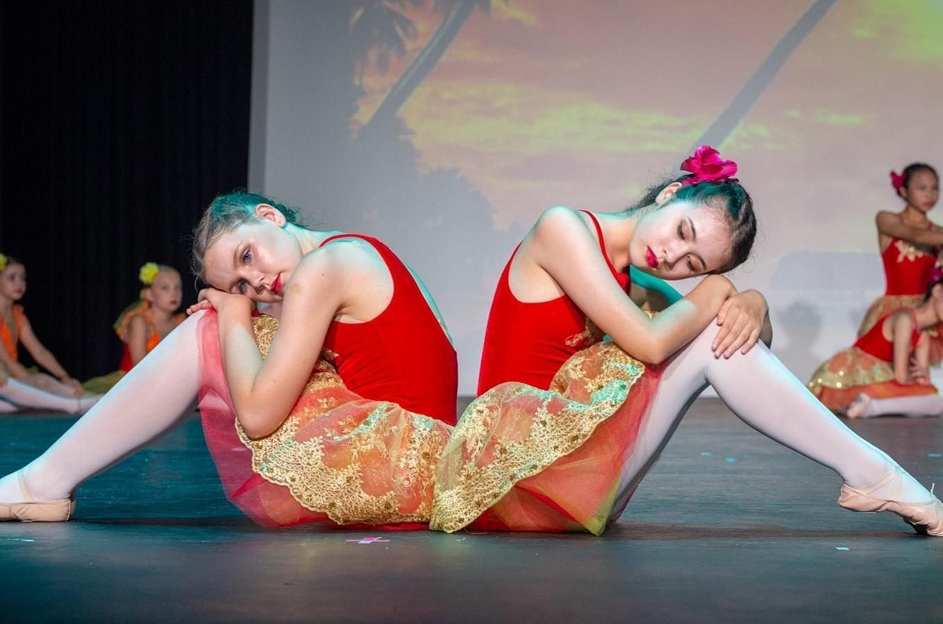 Two Young Dancers in Red Leotards and Gold Skirts Sit Back-to-back — Kay Flynn Dancing Academy Southport in Southport, QLD