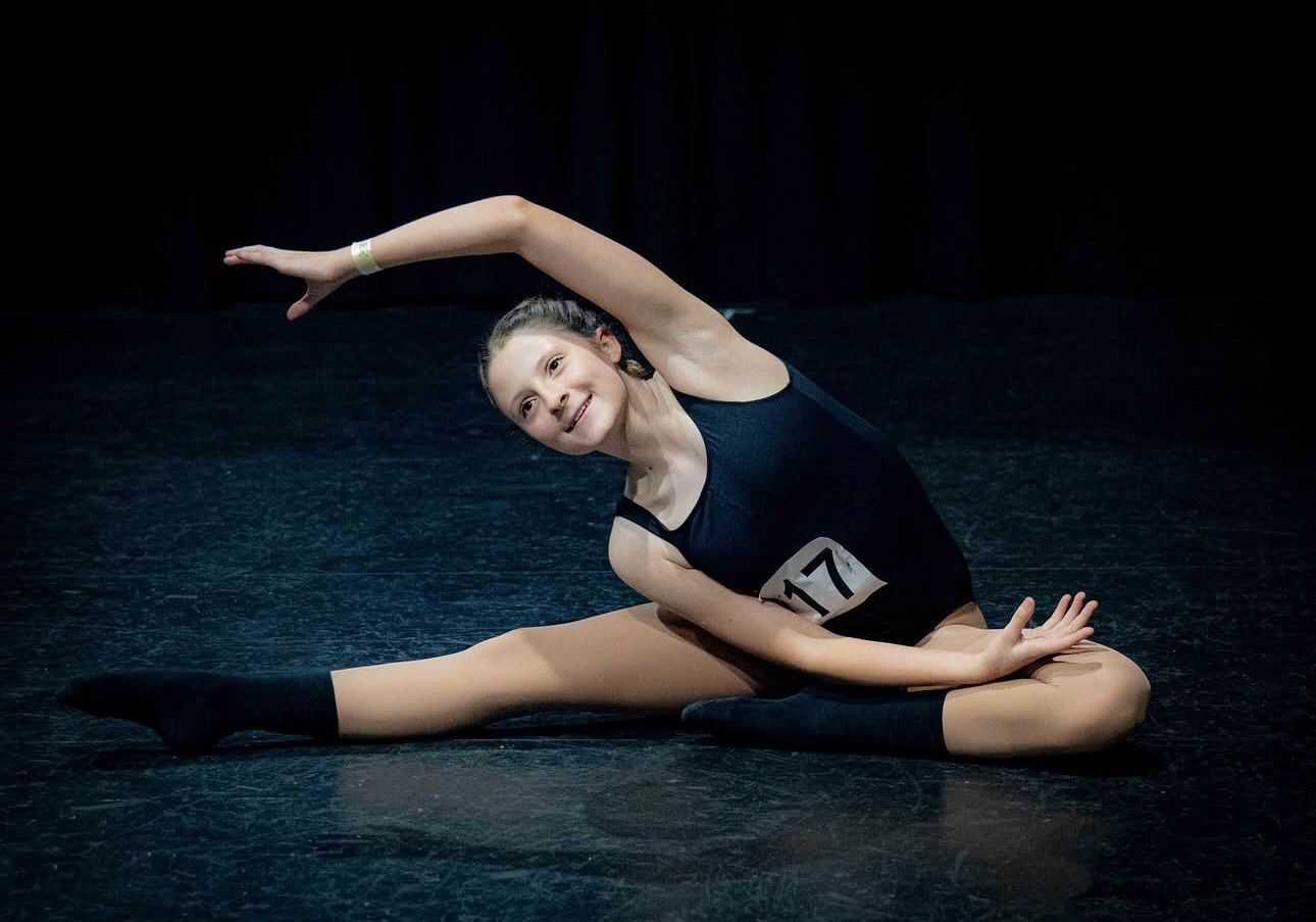 Young Dancer in Leotard Stretches on Stage, Smiling — Kay Flynn Dancing Academy Southport in Southport, QLD