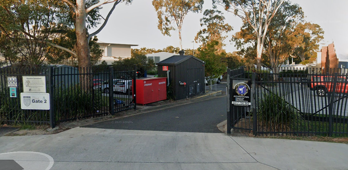 Entrance to a building complex with open black gates, a red contai ner, and a sign on the left. — Kay Flynn Dancing Academy Southport in Southport, QLD