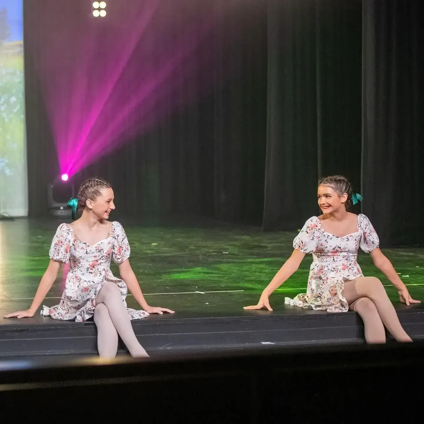 Two Young Dancers in Floral Dresses Sit on Stage, Smiling — Kay Flynn Dancing Academy Southport in Southport, QLD