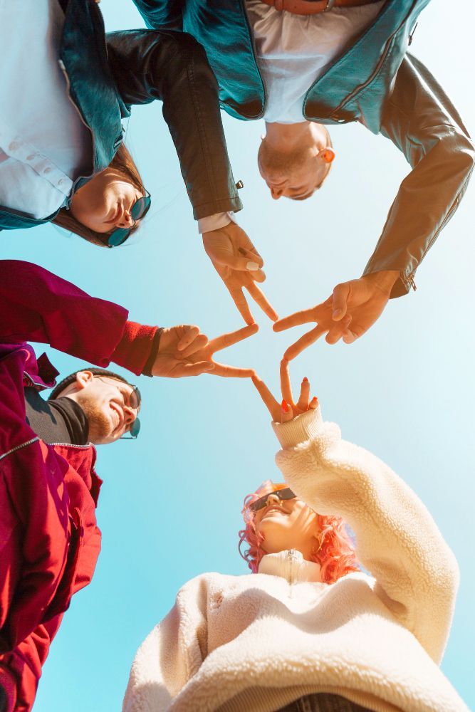 Five people making a star shape with their hands against a bright blue sky.