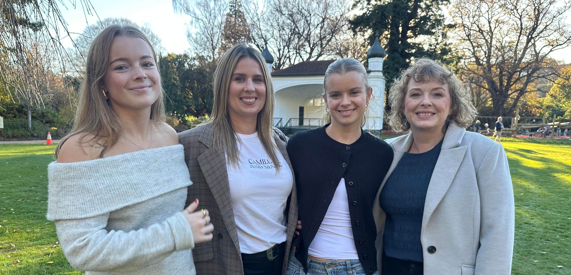Four people standing together in a park, smiling.