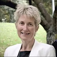 Woman with short, light hair wearing a white jacket smiles in an outdoor setting.